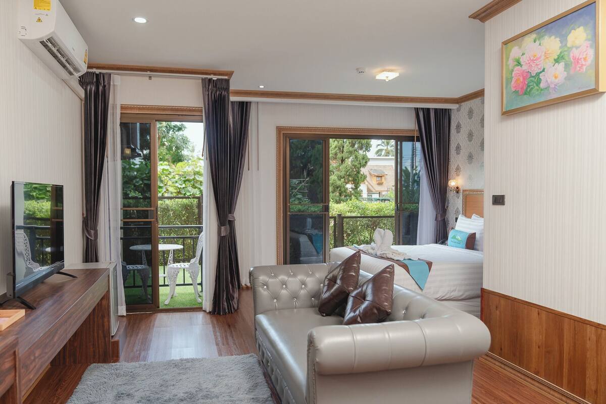 A modern living room with a sofa, a TV, and a balcony with outdoor seating.