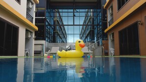 A swimming pool with a yellow inflatable duck, surrounded by lounge chairs and a modern building in the background. - Baan Plaifah Khao Yai Hotel (Pak Chong)