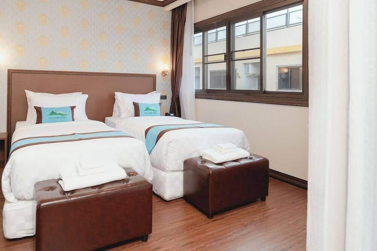 A hotel room with two beds, a window, and a wooden floor.