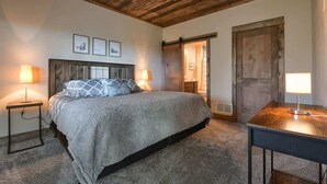 Ein Schlafzimmer mit Holzboden, einem Bett mit grauer Decke, zwei Nachttischlampen und einer Holztür.