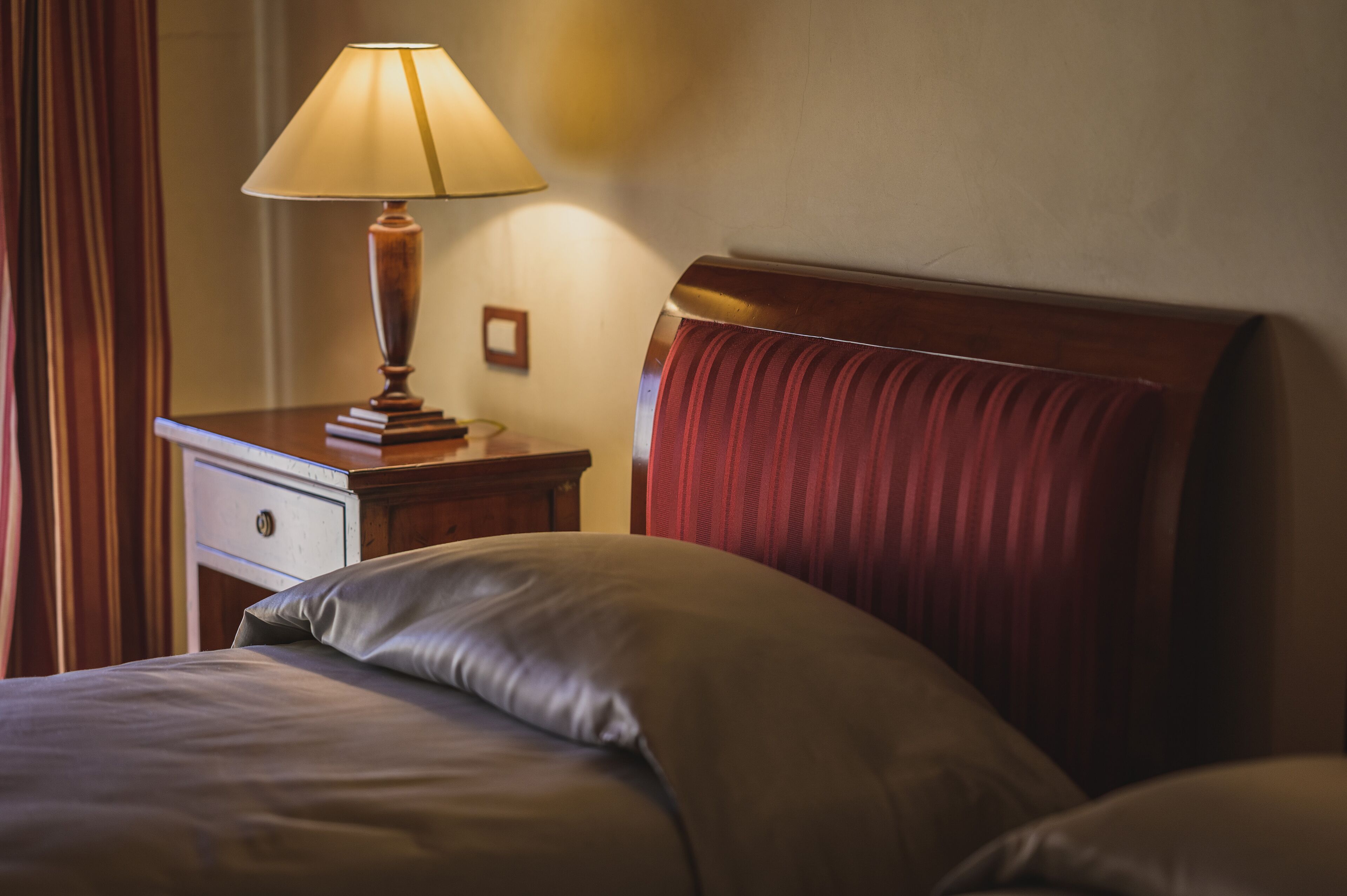 Habitació d'hotel amb una petita taula de nit de fusta, una làmpada i un llit amb capçalera.