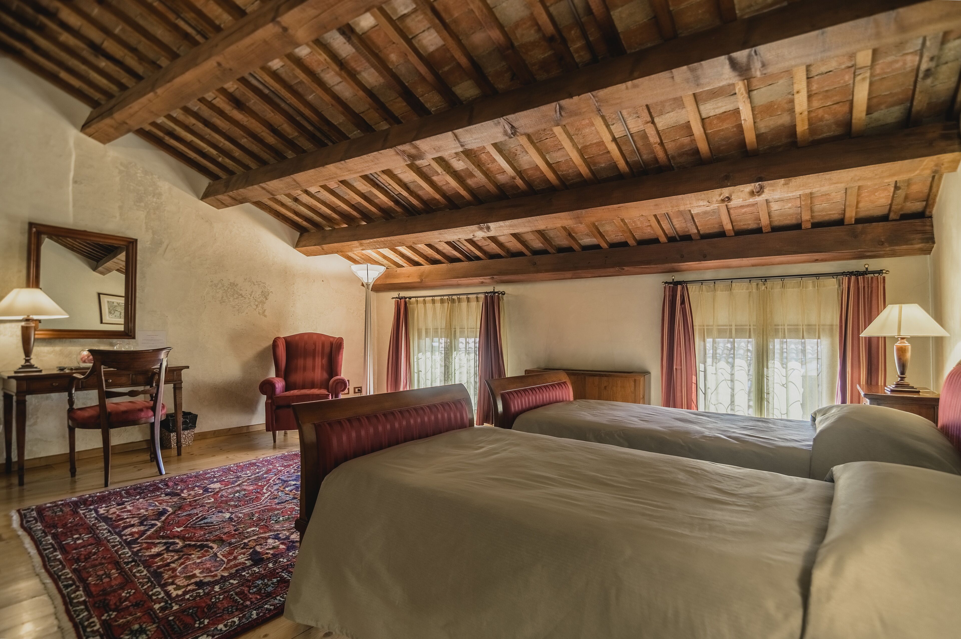 A room with a wooden ceiling, two beds, a chair, a desk, and a rug.
