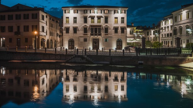 Un bâtiment historique doté d’une cour intérieure, de fenêtres en arc de cercle et dont l’image se reflète dans l’eau.