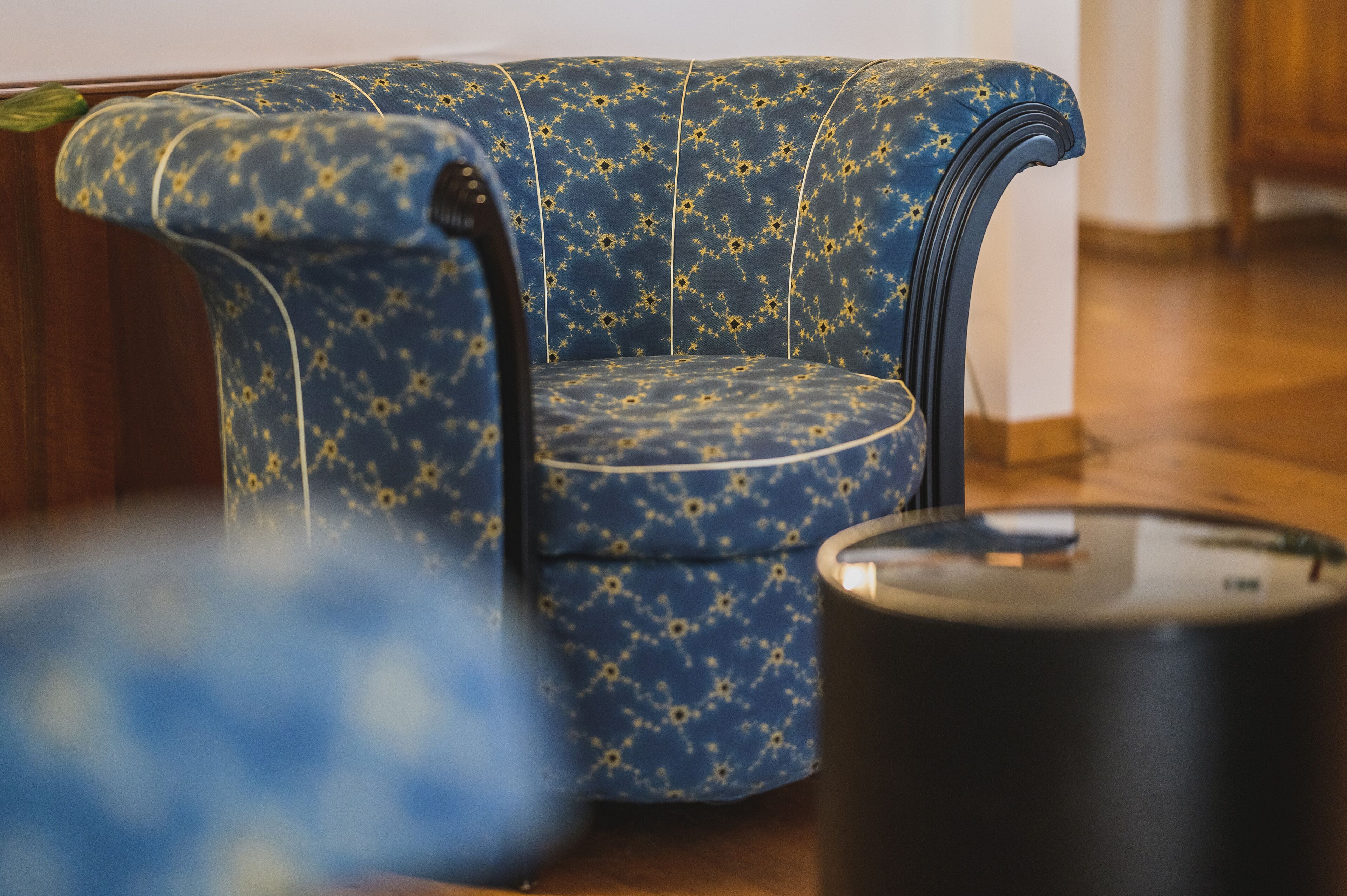 A blue upholstered chair with a geometric pattern, a black side table, and a wooden floor.