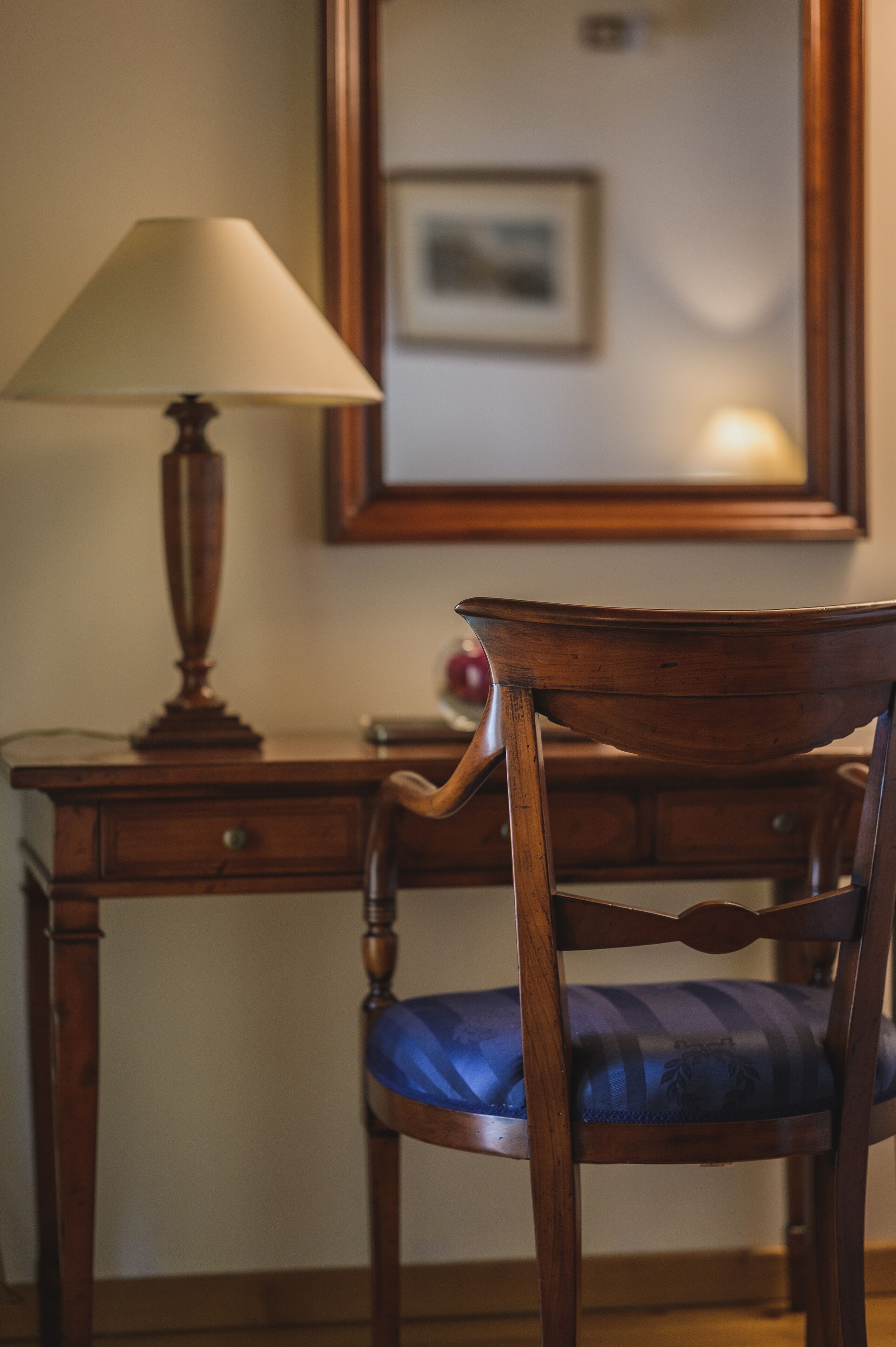 A wooden desk with a lamp and a chair with a cushion.