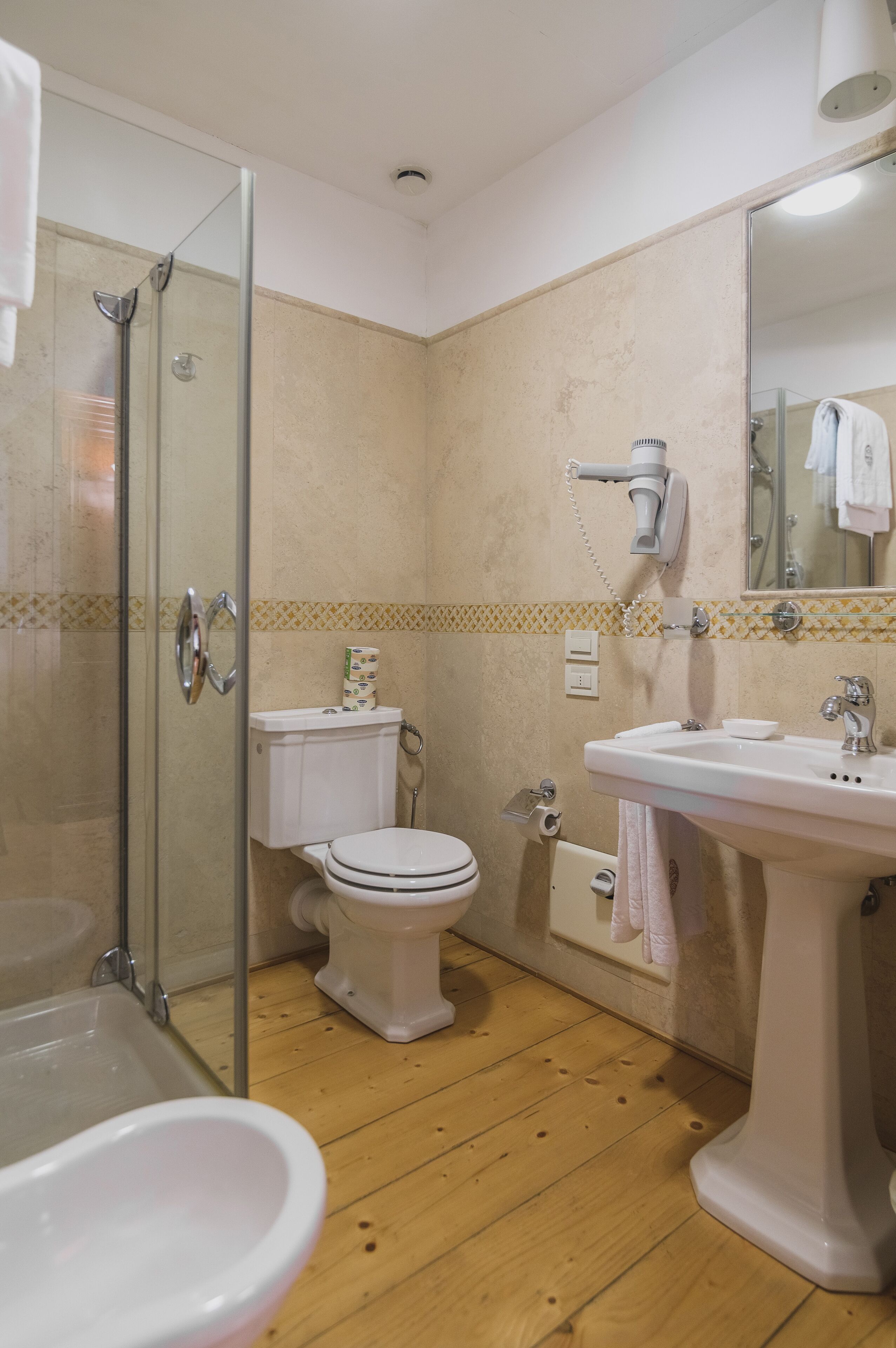 A bathroom with a glass shower enclosure, a toilet, a sink, and a hairdryer mounted on the wall.