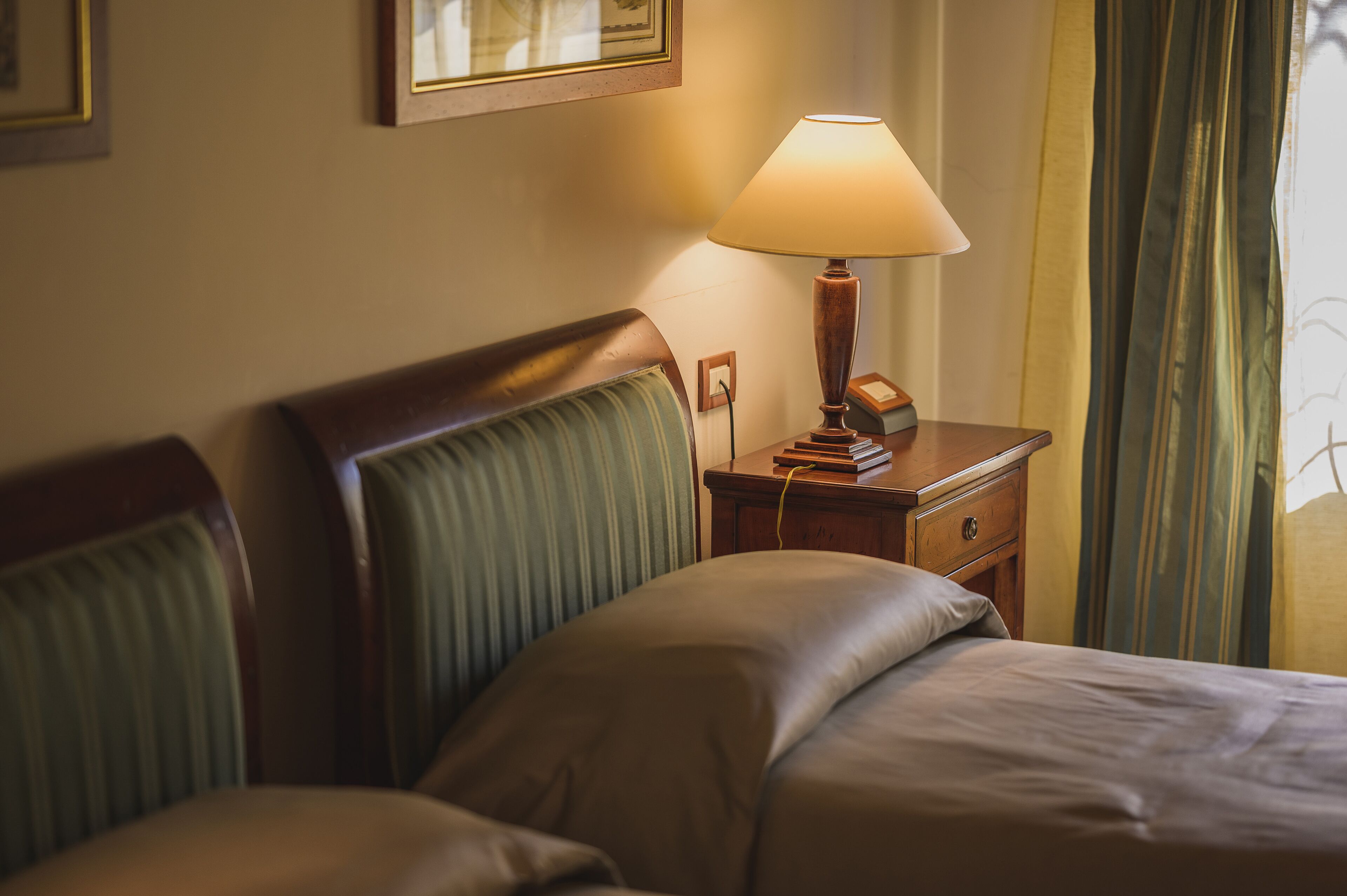 A hotel room with a bed, a nightstand with a lamp, and a framed picture on the wall.