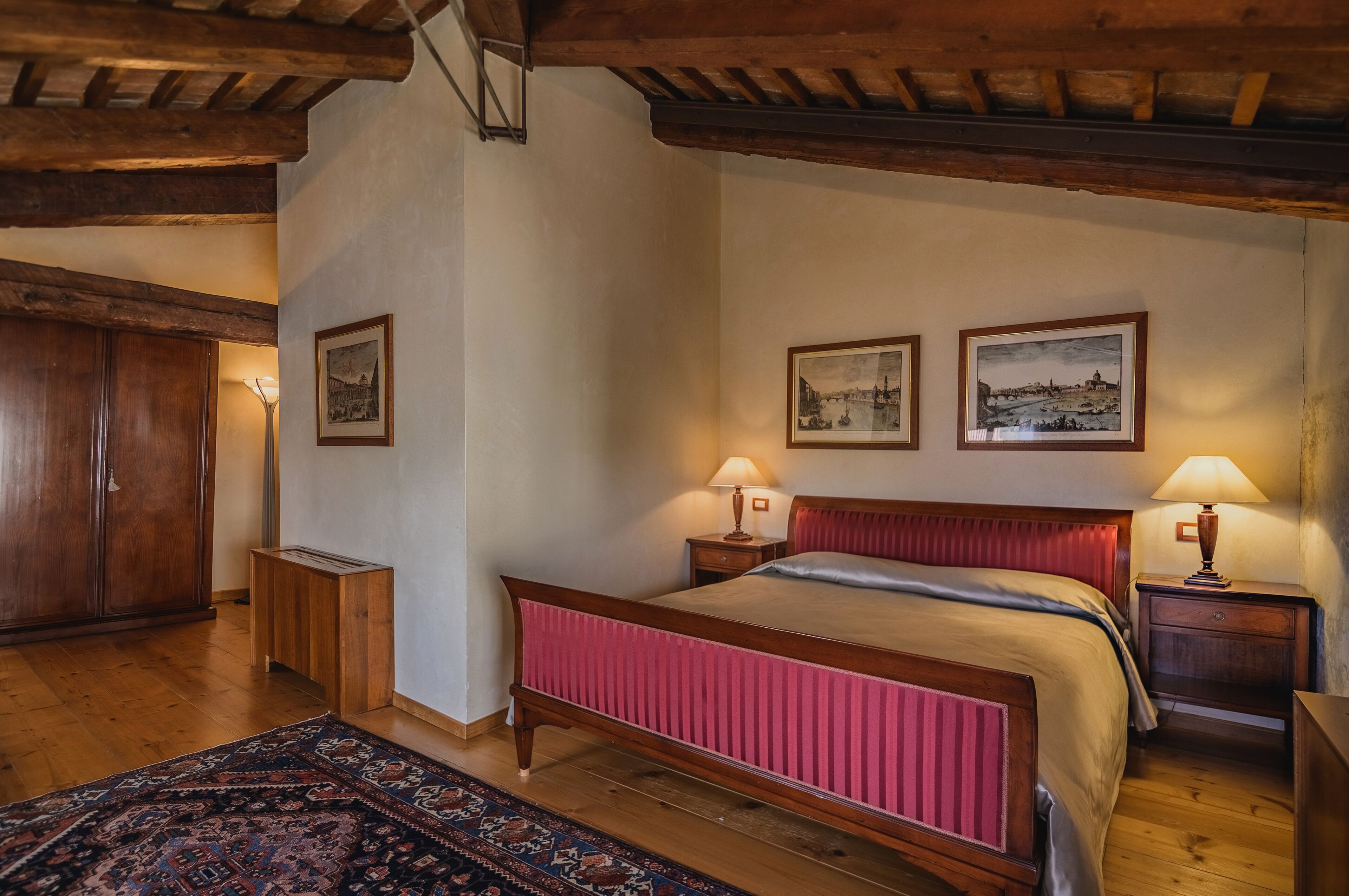 A bedroom with a wooden bed, two bedside tables with lamps, a wooden wardrobe, and two framed pictures on the wall.