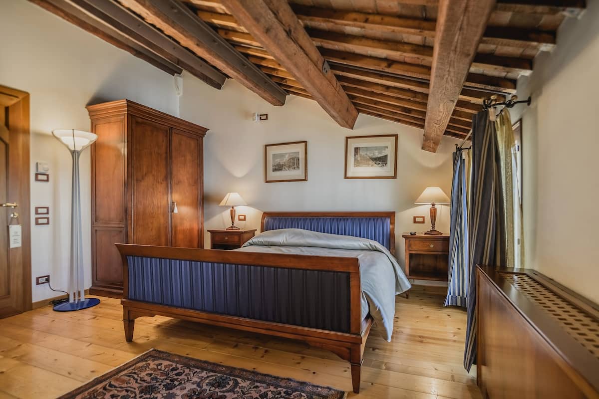 Een slaapkamer met een houten bed, een garderobe, twee nachtkastjes met lampen, een radiator en een raam met gordijnen.