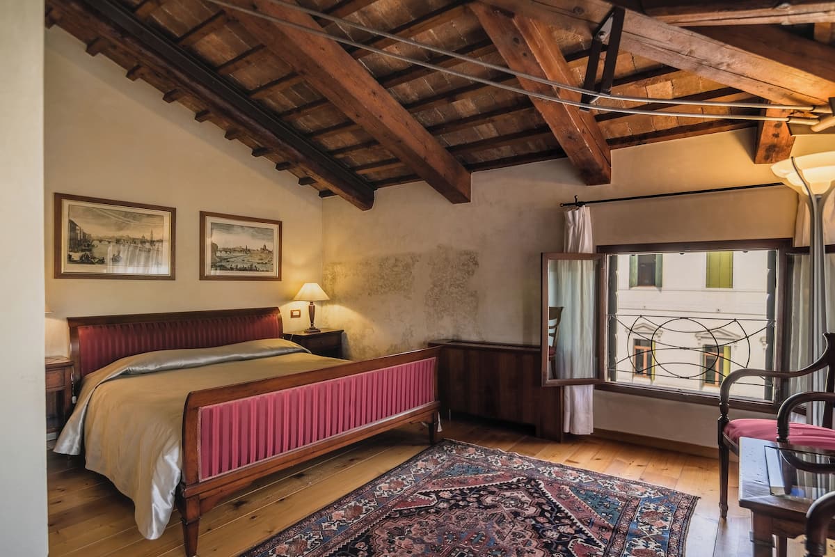 Een slaapkamer met een houten bed, een raam met uitzicht en een kamerbreed tapijt met dessin.