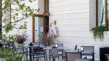 Un café en plein air avec des tables et des chaises, une enseigne indiquant « CAFFÈ LETTERARO » et des plantes en pot.