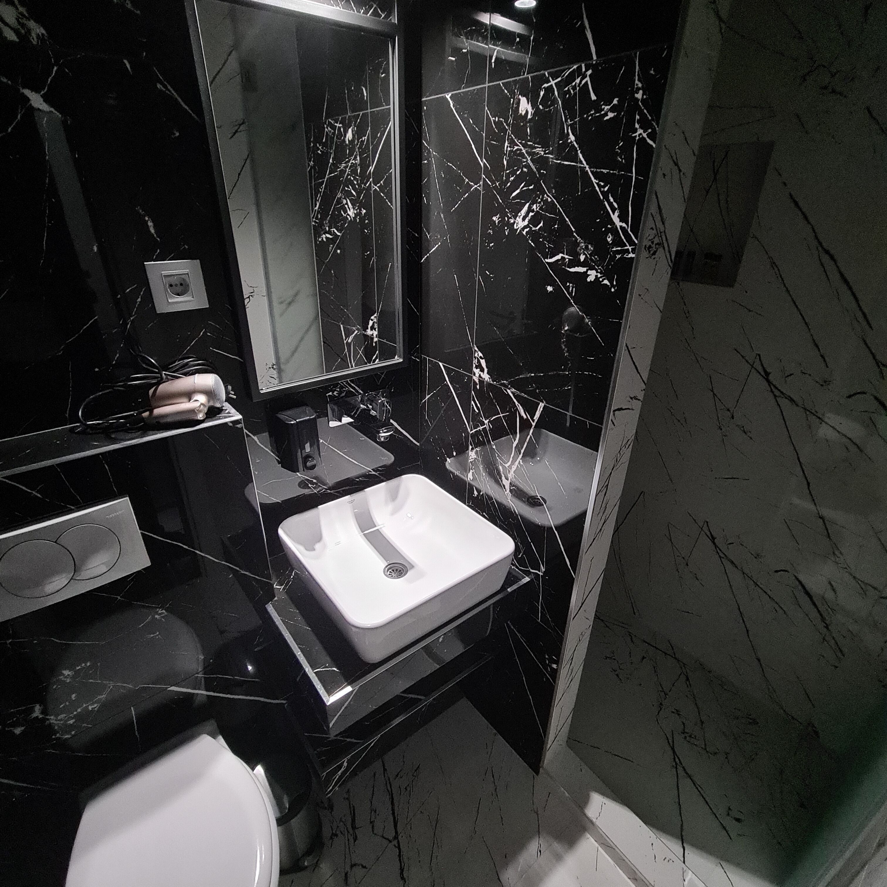 A bathroom with a white sink, a mirror, and a black marble wall.