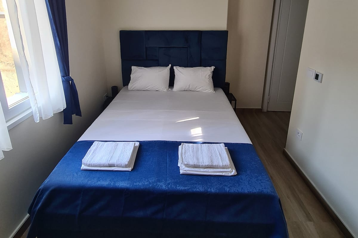 Una cama bien hecha con un cabecero azul, ropa de cama blanca y dos toallas dobladas al pie de la cama.