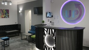 A reception area with a modern design, including a black reception desk, a blue sofa, and a green chair. - UP accommodation (Belgrade)