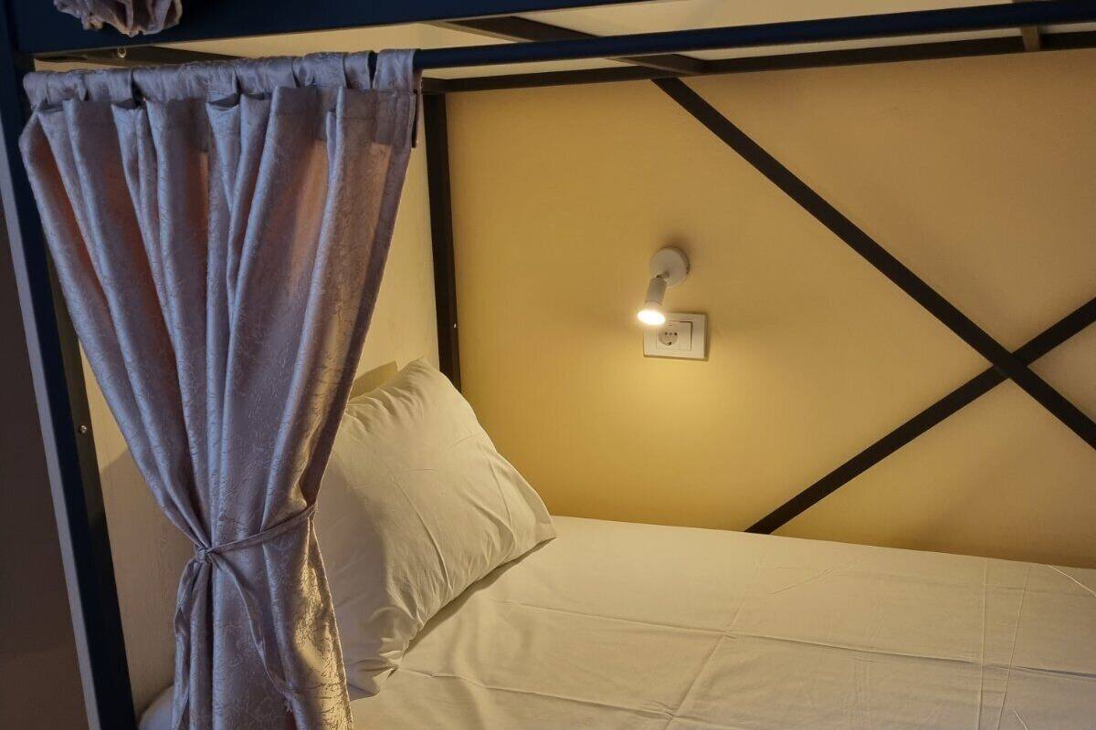 Una cama litera con cortina, una lámpara de noche y una luz fijada en la pared.