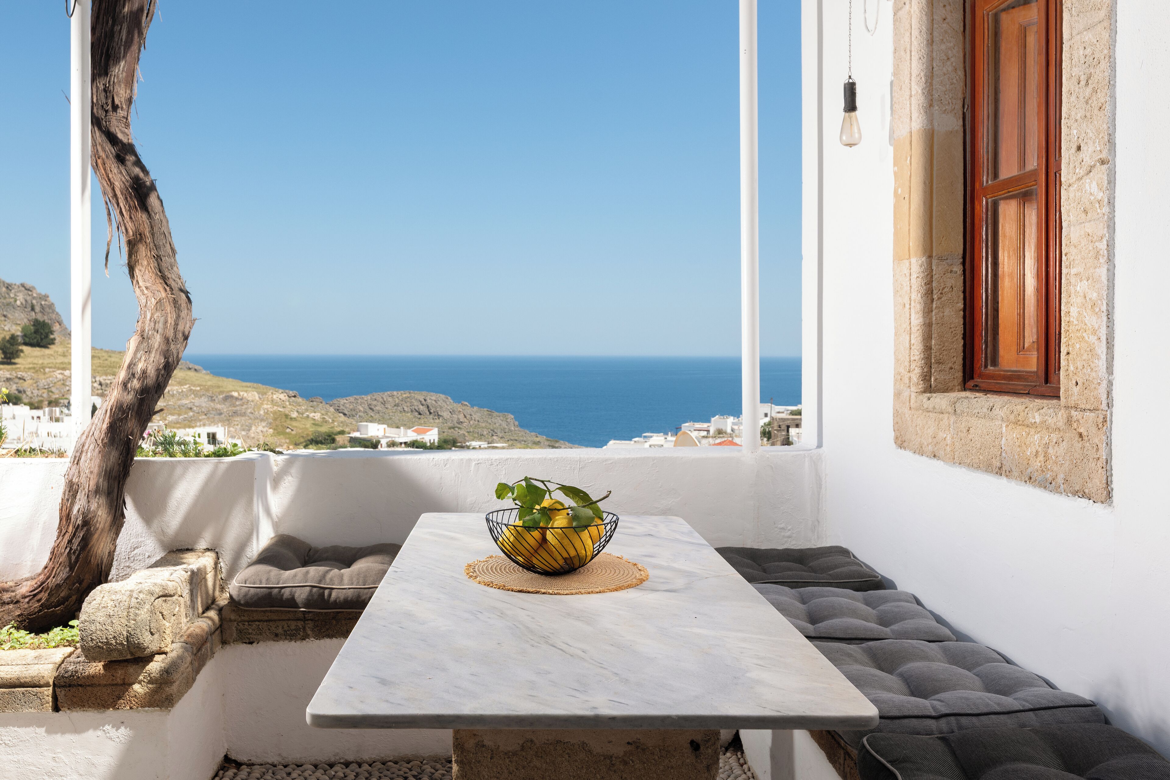 A balcony with a table, a bowl with lemons, and a view of the sea.