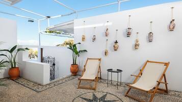 Una habitación iluminada por el sol, con una pared blanca, dos sillas de madera, una mesita y jarrones decorativos.