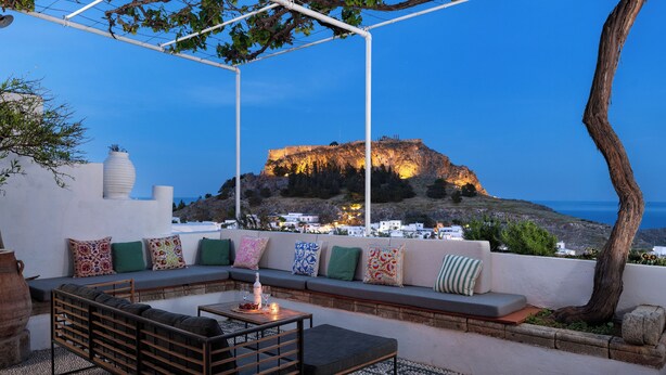 Una terrazza con vista su una fortezza collinare, un'area salotto con cuscini e un tavolo con una bottiglia.