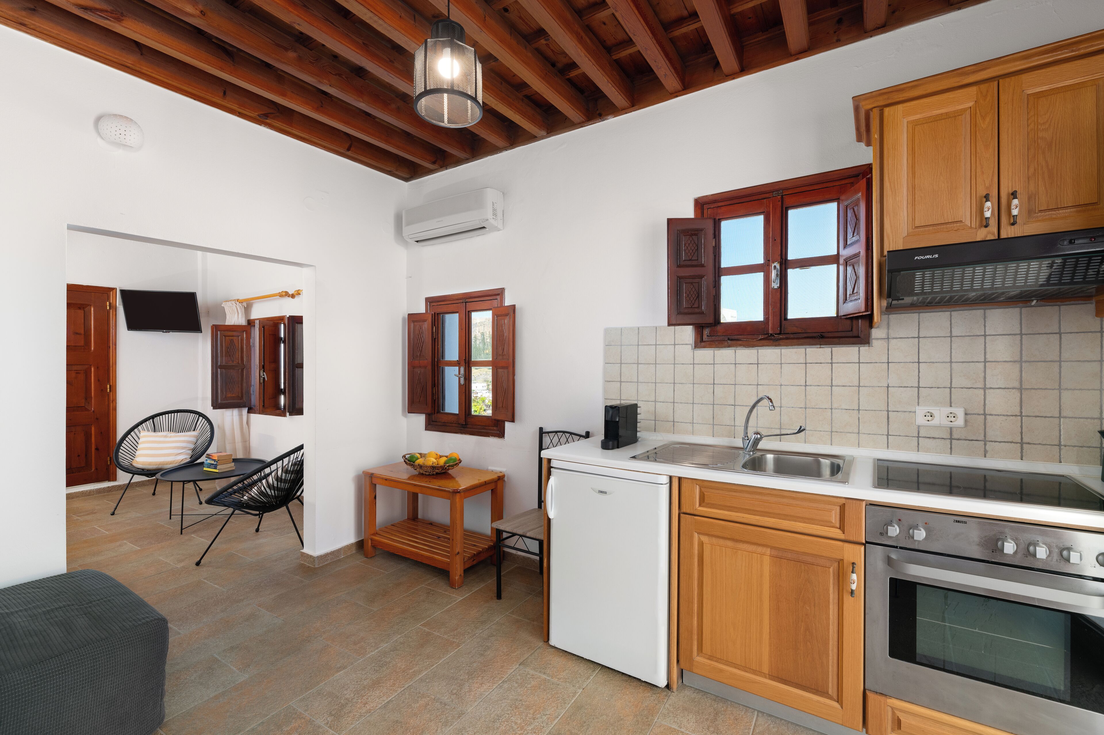 A compact kitchen with wooden cabinets, a built-in oven, a sink, and a small dining area with chairs and a table.