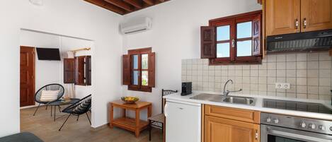 A compact kitchen with wooden cabinets, a built-in oven, a sink, and a small dining area with chairs and a table.