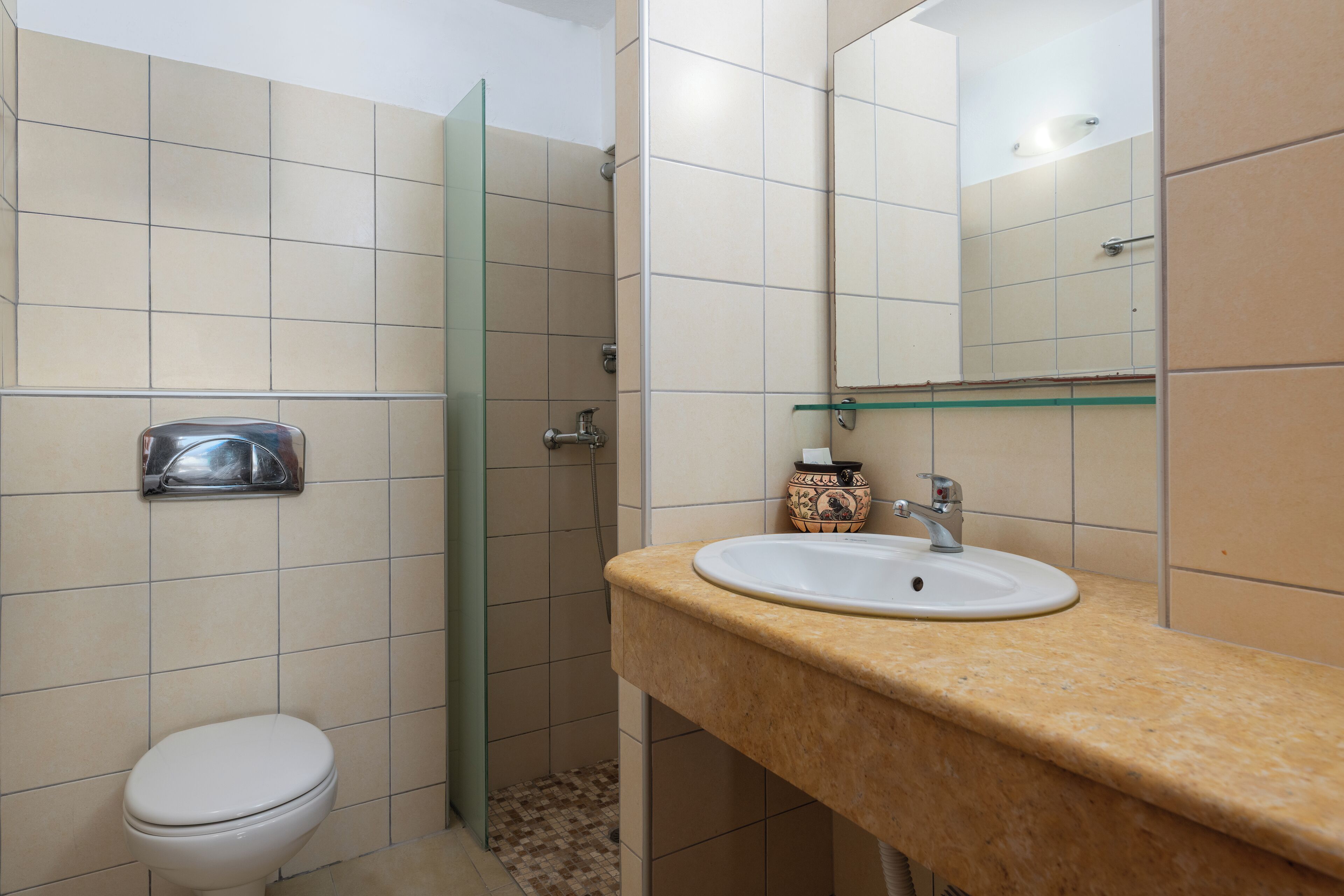 A bathroom with a toilet, sink, mirror, and shower.