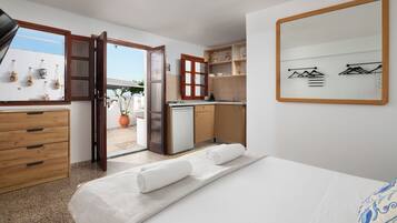 Un dormitorio con cama, cómoda de madera, zona de cocina y un espejo grande.
