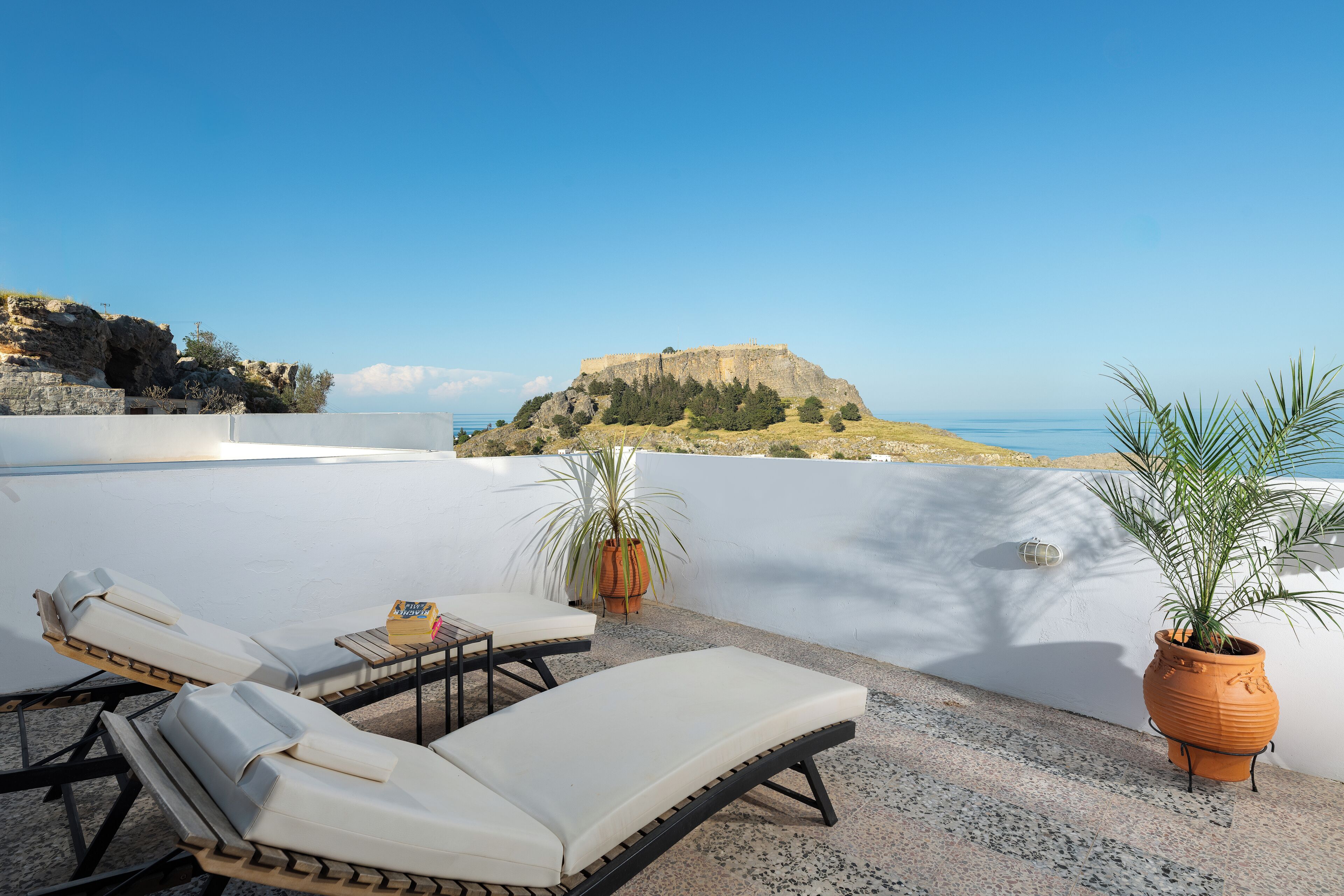A rooftop terrace with lounge chairs, a potted plant, and a view of a coastal landscape.