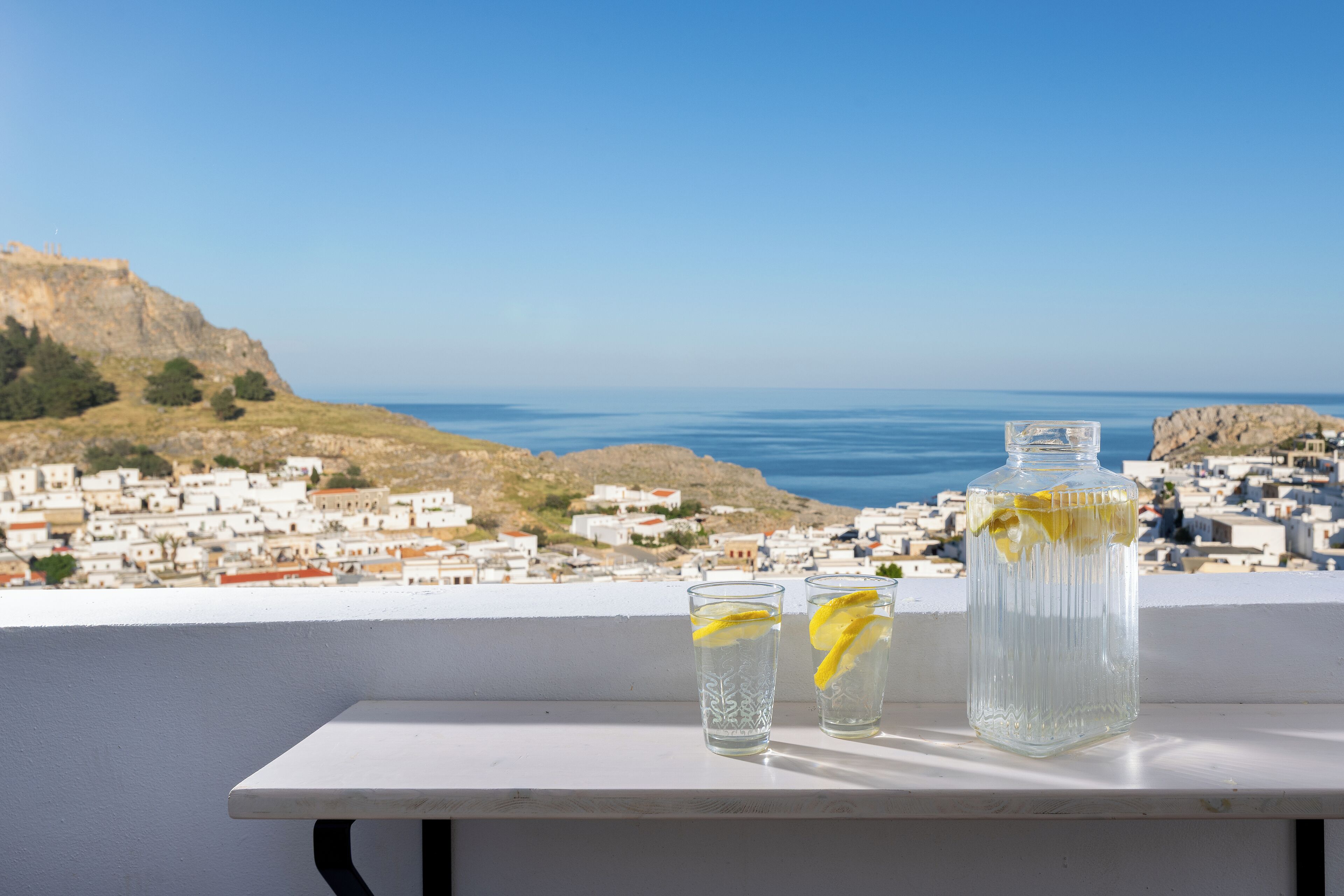A table with two glasses and a bottle on a balcony overlooking a coastal town.