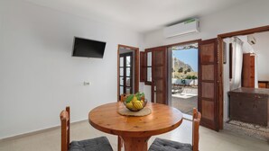 Zona pranzo con tavolo rotondo in legno, due sedie, una ciotola di frutta e un televisore appeso al muro.
