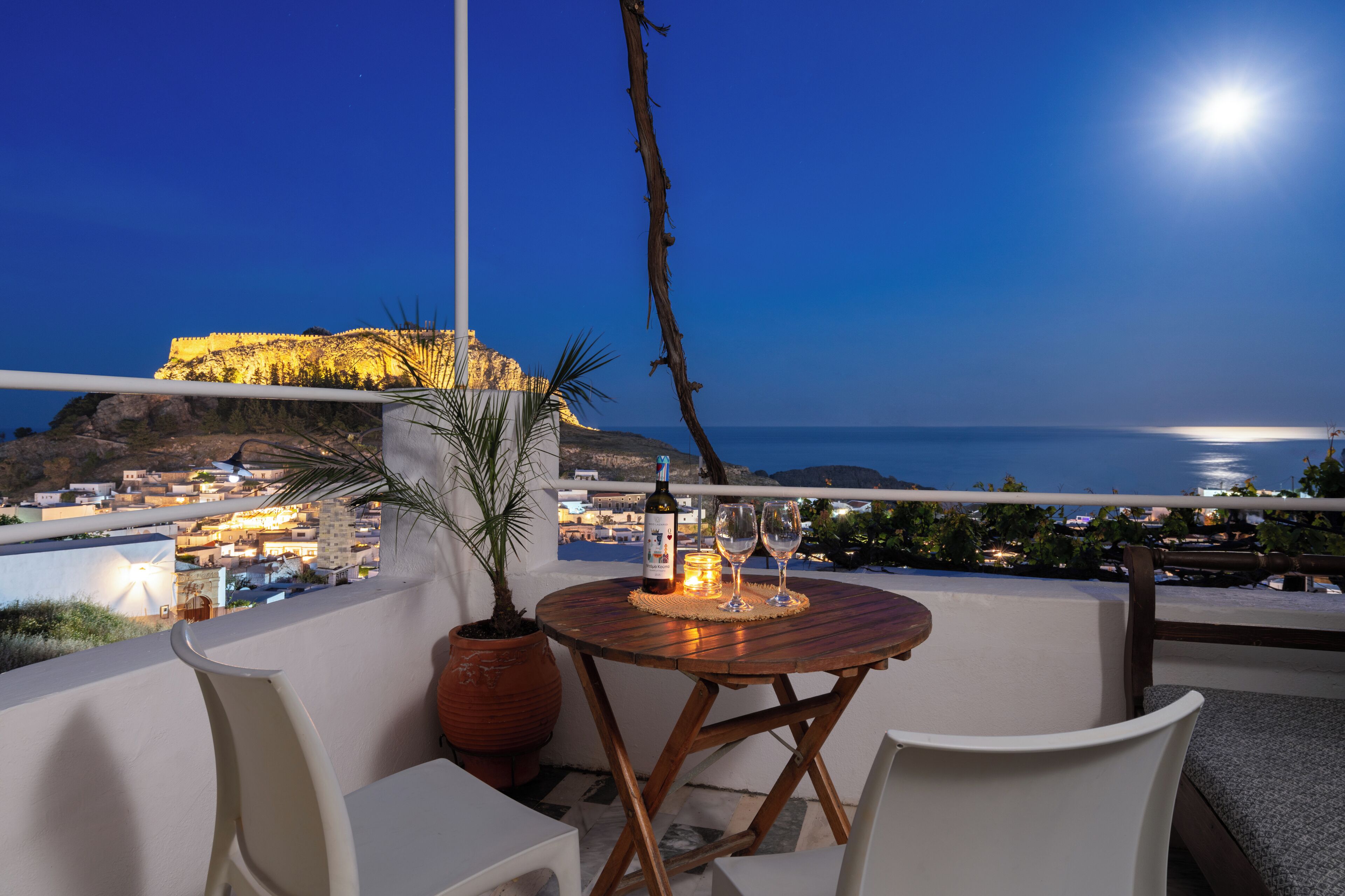 A balcony with a table, chairs, a potted plant, and a bottle of wine.
