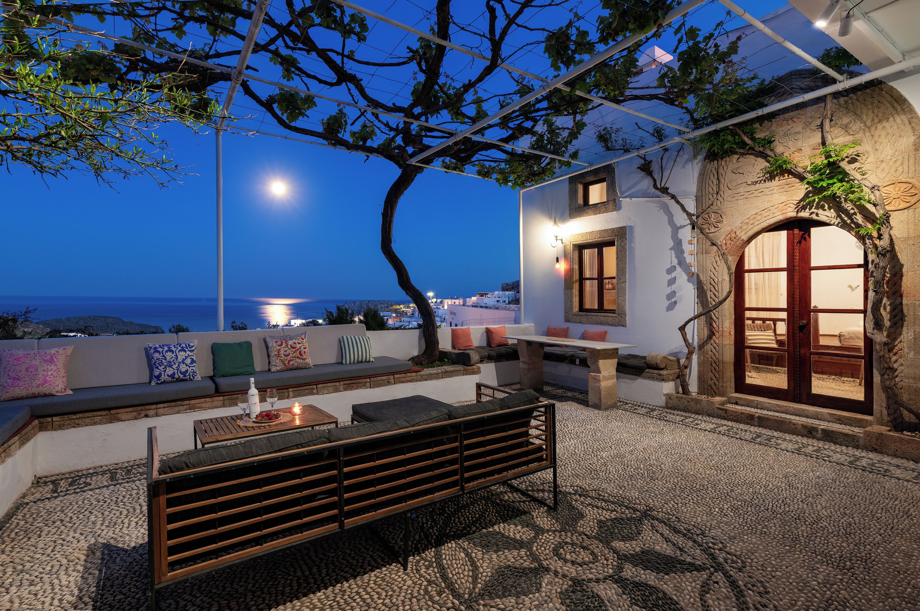 A rooftop terrace with a wooden bench, a table, and a sofa with cushions.