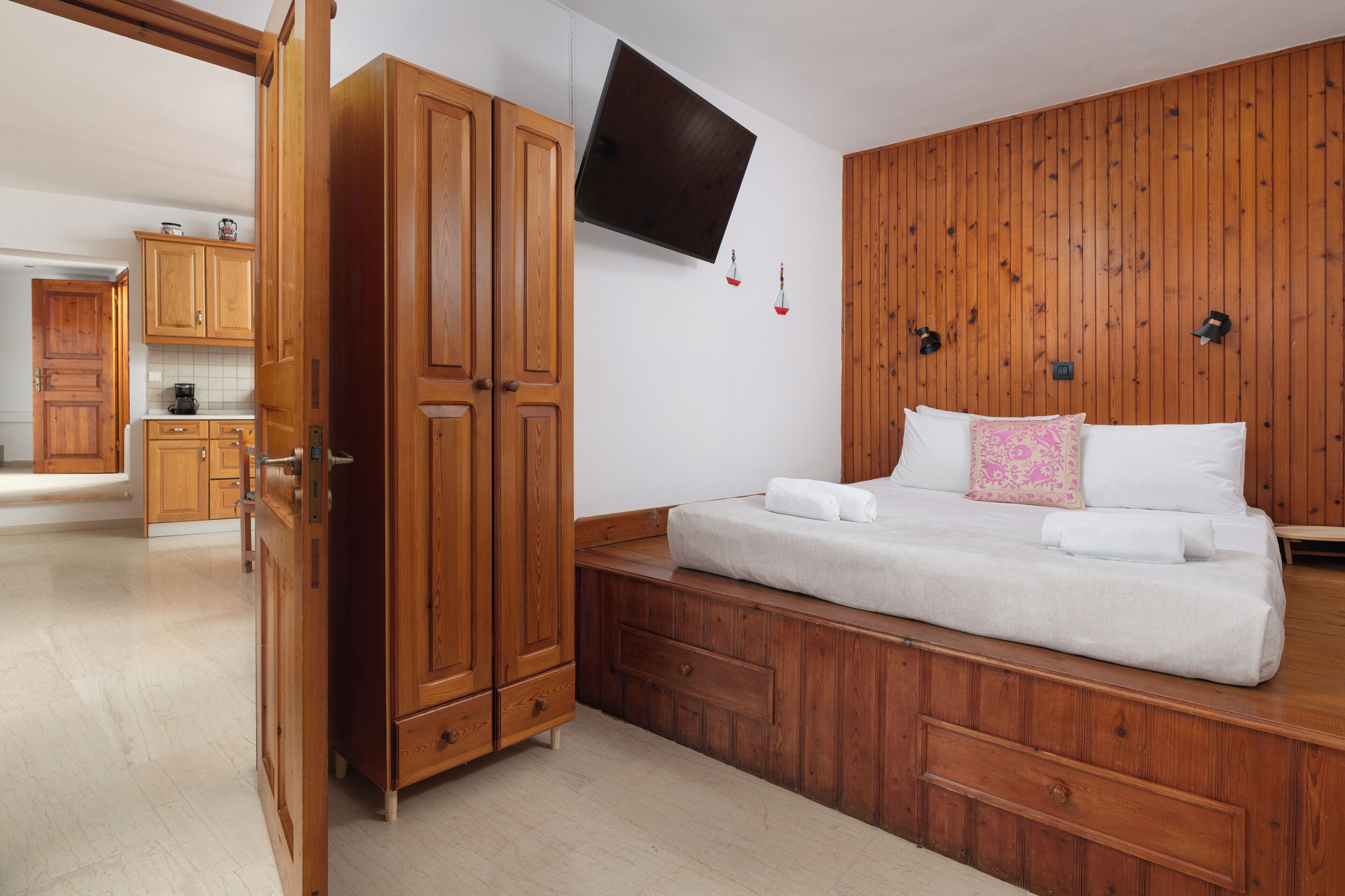 A bedroom with a bed, wooden wardrobe, and a TV mounted on the wall.