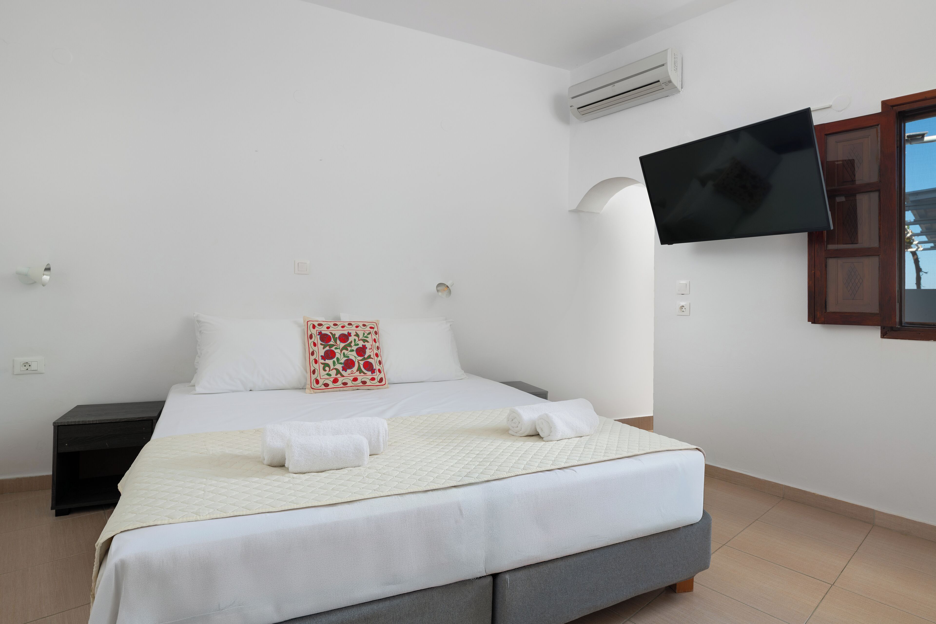 A bedroom with a bed, a flat-screen TV mounted on the wall, and a nightstand.