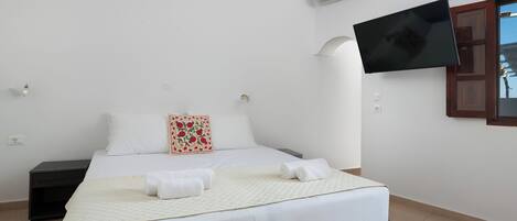 A bedroom with a bed, a flat-screen TV mounted on the wall, and a nightstand.
