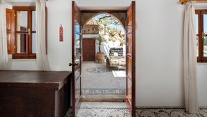 Una porta aperta che dà su un cortile con pavimento decorato, una panca di legno e una pianta in vaso.