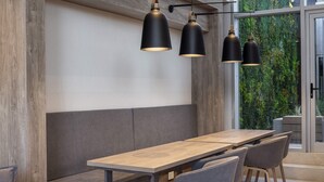 A modern dining area with a long wooden table, grey upholstered seating, and black pendant lights. - Dots del Alto (Neuquén)