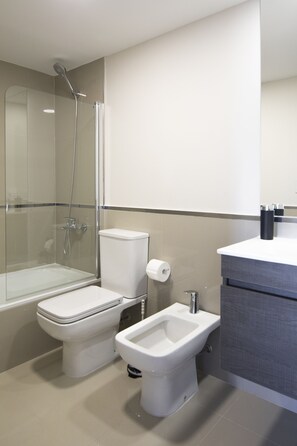 Un baño moderno con ducha de vidrio, inodoro, bidé y tocador con espejo.