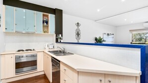 A modern kitchen with light blue cabinets, a white countertop, stainless steel appliances, and decorative wall art. - Island Vibes Retreat on the Cowes Esplanade (Cowes)