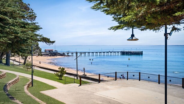 A coastal walkway with a pier extending into the water, a beach, and a grassy area with trees. - Island Vibes Retreat on the Cowes Esplanade (Cowes)