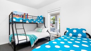A bunk bed room with a polka dot bedspread, a view of the street through a window, and a small table with a lamp. - Island Vibes Retreat on the Cowes Esplanade (Cowes)