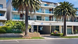A beachfront hotel with a modern design, featuring balconies, palm trees, and a sign indicating it is a daily accommodation. - Island Vibes Retreat on the Cowes Esplanade (Cowes)