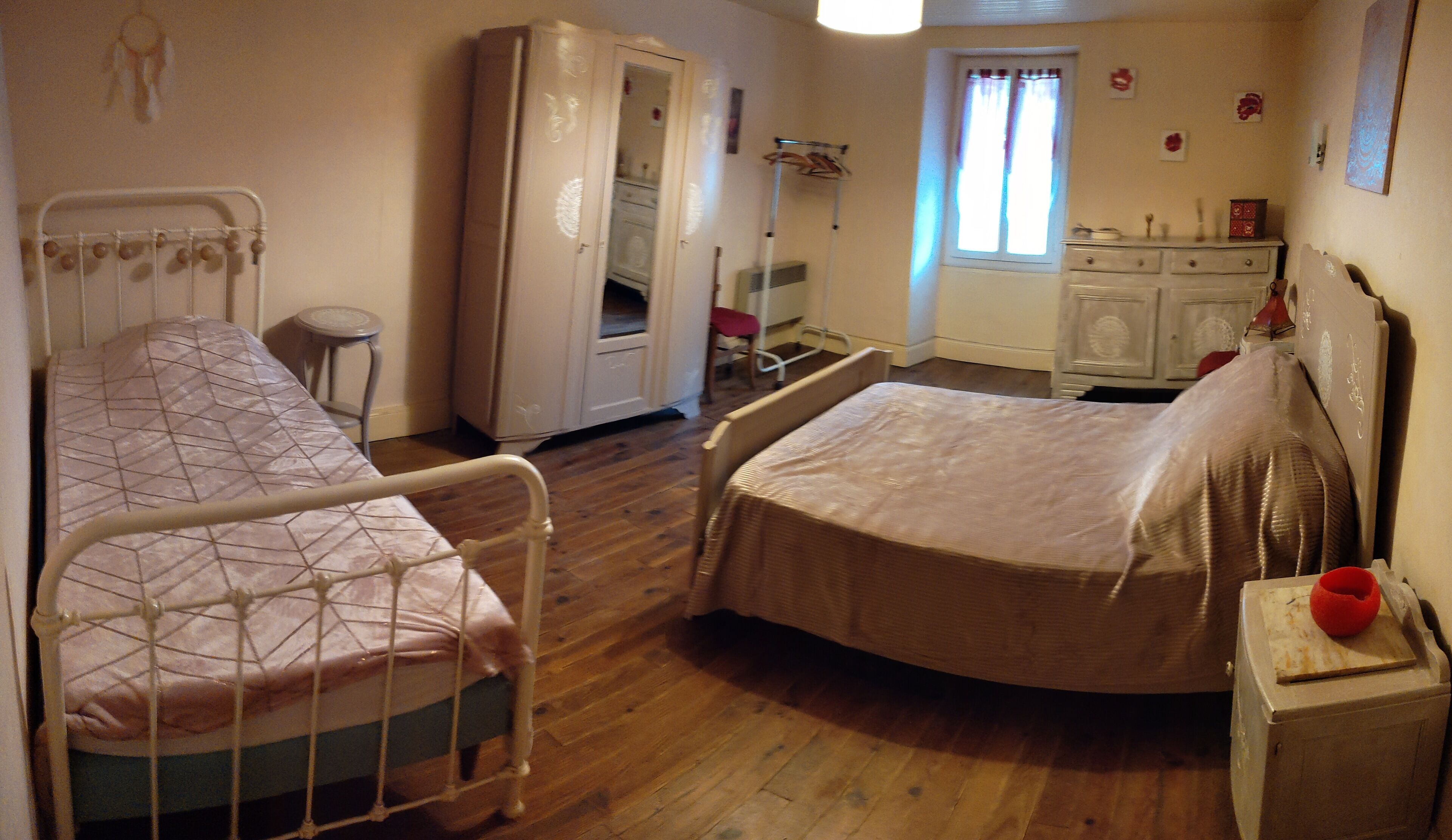 Une chambre avec deux lits, une armoire, une fenêtre avec des rideaux et une table de chevet sur laquelle se trouve un objet rouge.