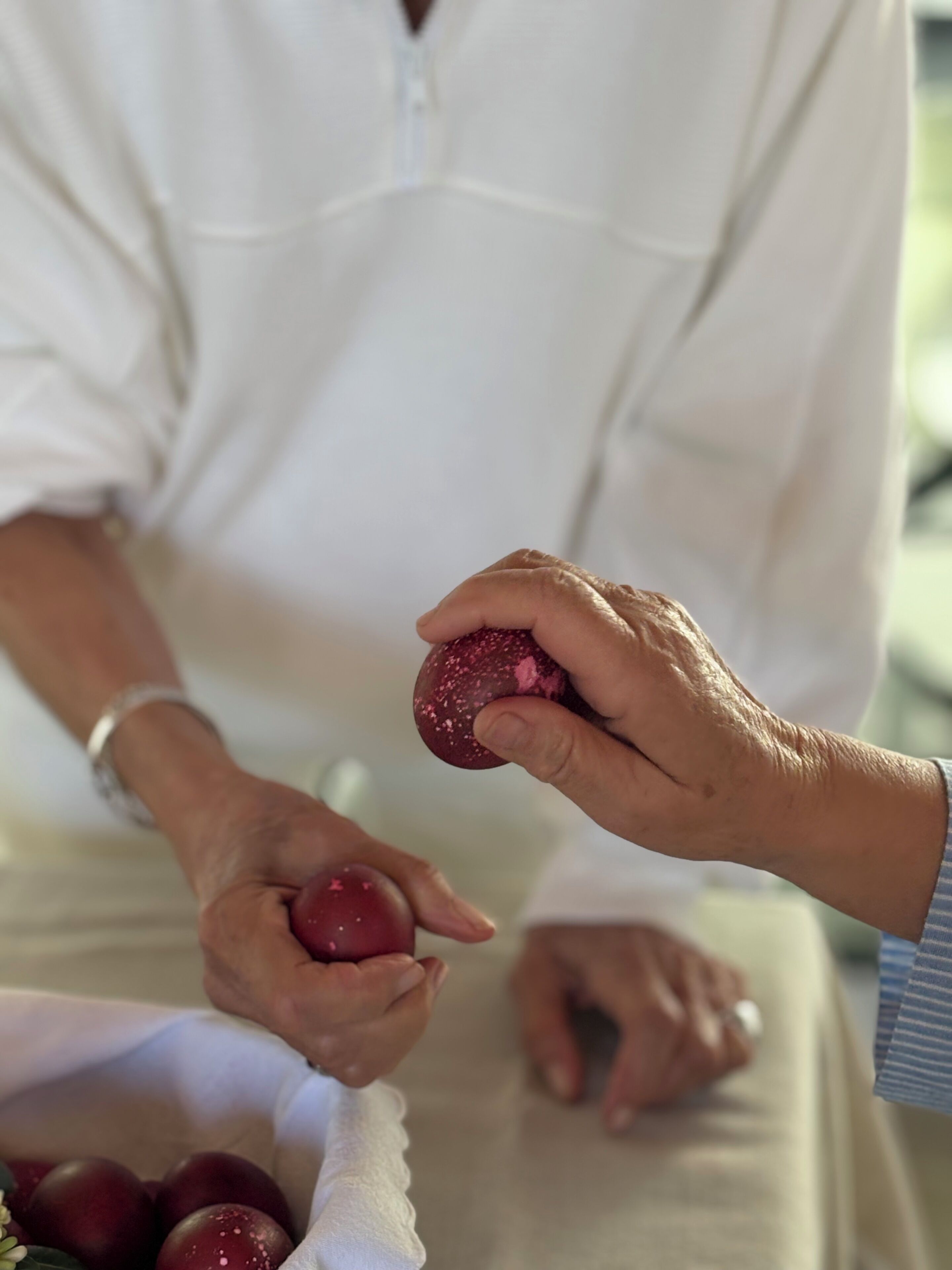 Iemand houdt een rood stuk fruit vast, mogelijk een pruim, terwijl een andere hand ernaar reikend is.