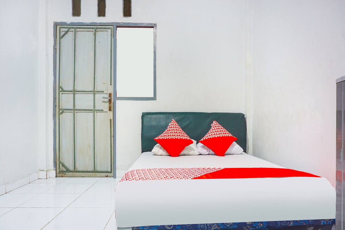 A bed with a white and red patterned bedspread, two red pillows with a white pattern, and a green headboard.