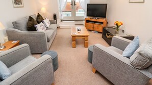 Uma sala de estar moderna com sofás cinzas, uma mesa de centro de madeira, uma TV em um suporte de madeira e uma varanda com vista.