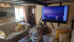 A cozy living room with striped sofas, a wooden coffee table, and a flat-screen TV displaying a sunset scene.