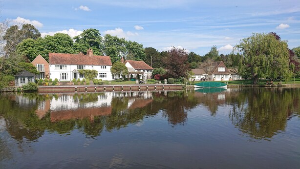 A serene lakeside view with a row of white buildings, a covered boathouse, and a small dock.