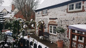 A snow-covered courtyard with a rustic building, a bench, and a 'No Parking' sign.