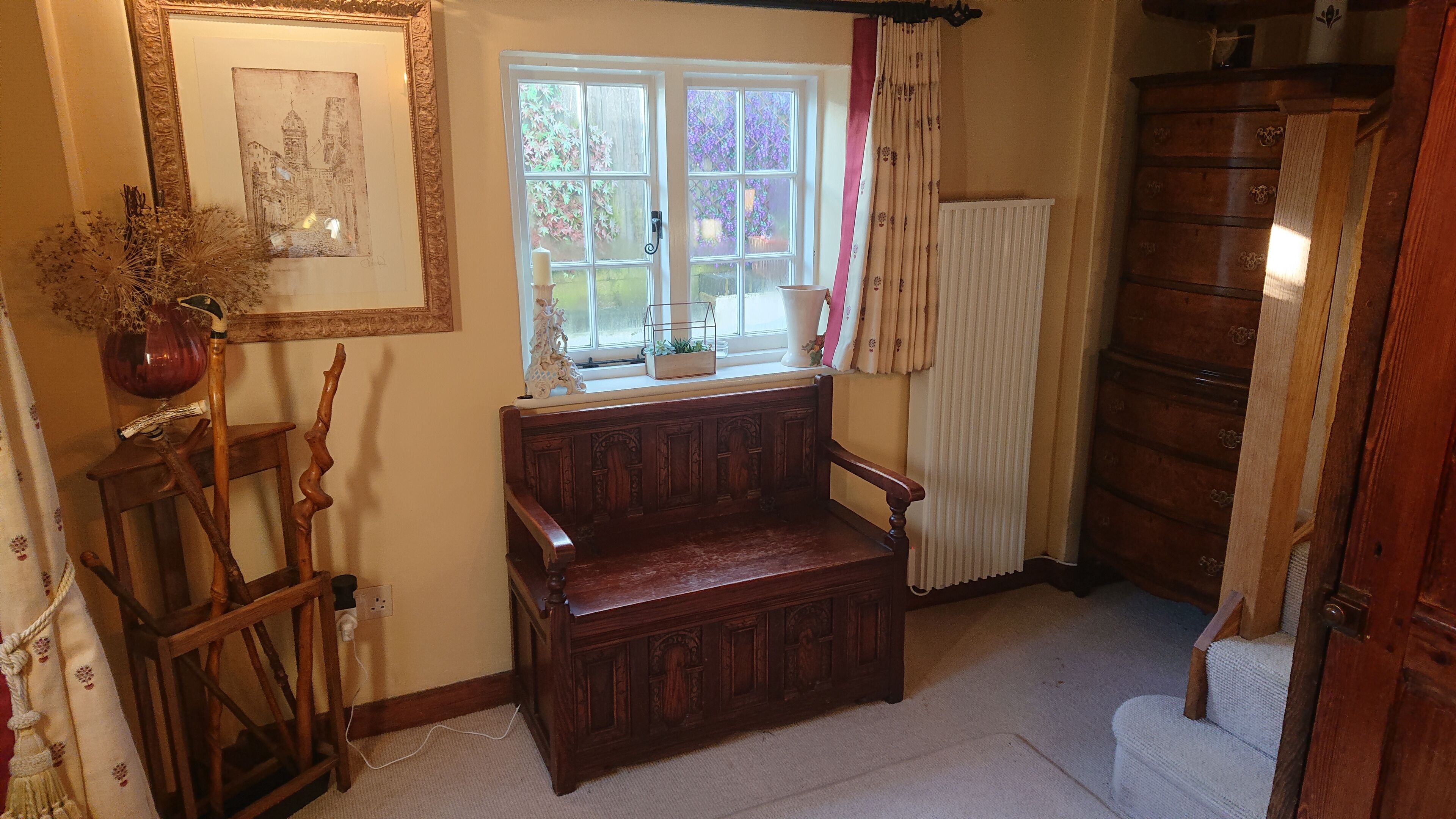 Una habitación acogedora con un banco de madera, una ventana con cortinas, un radiador y un armario de madera.