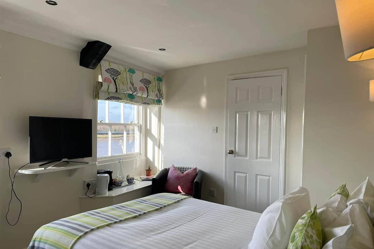 A bedroom with a bed, a television on a stand, a window with curtains, and a door.